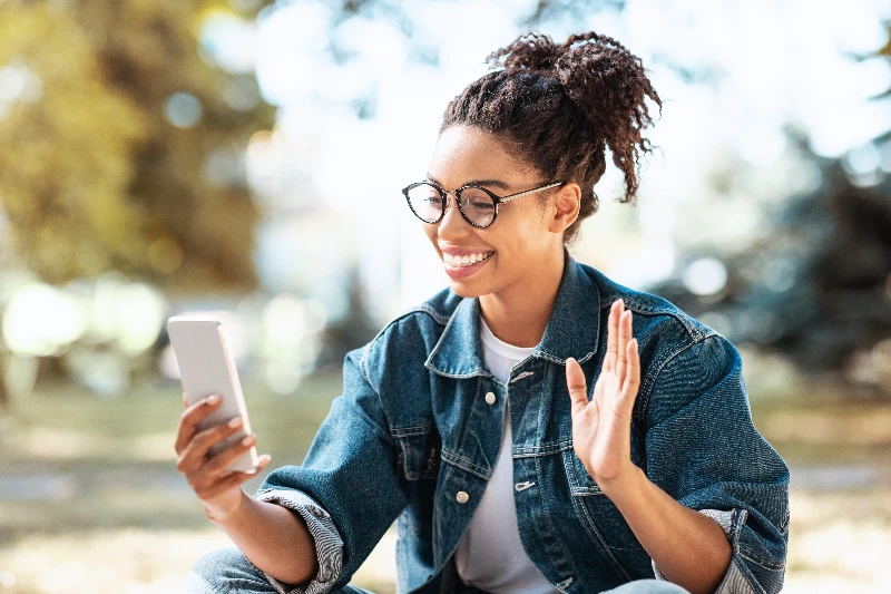 Happy Woman Using Smartphone Making Video Call Sitting In Park Outside